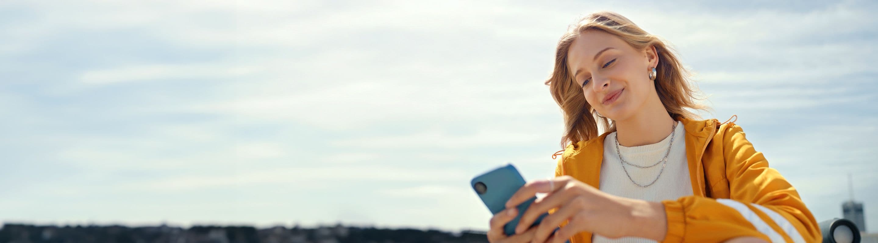 Ung kvinne sitter ut og ser på mobilen mens hun smiler