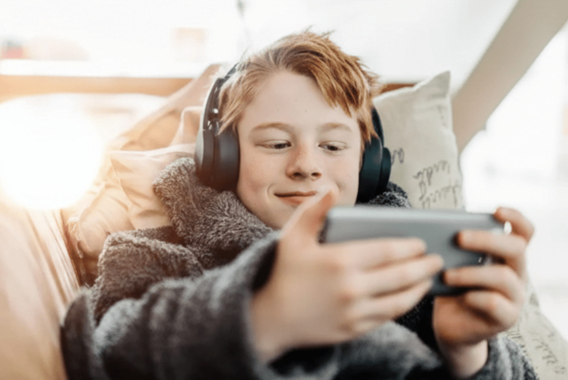 Ung gutt ligger på sofaen med headset og ser på mobilen