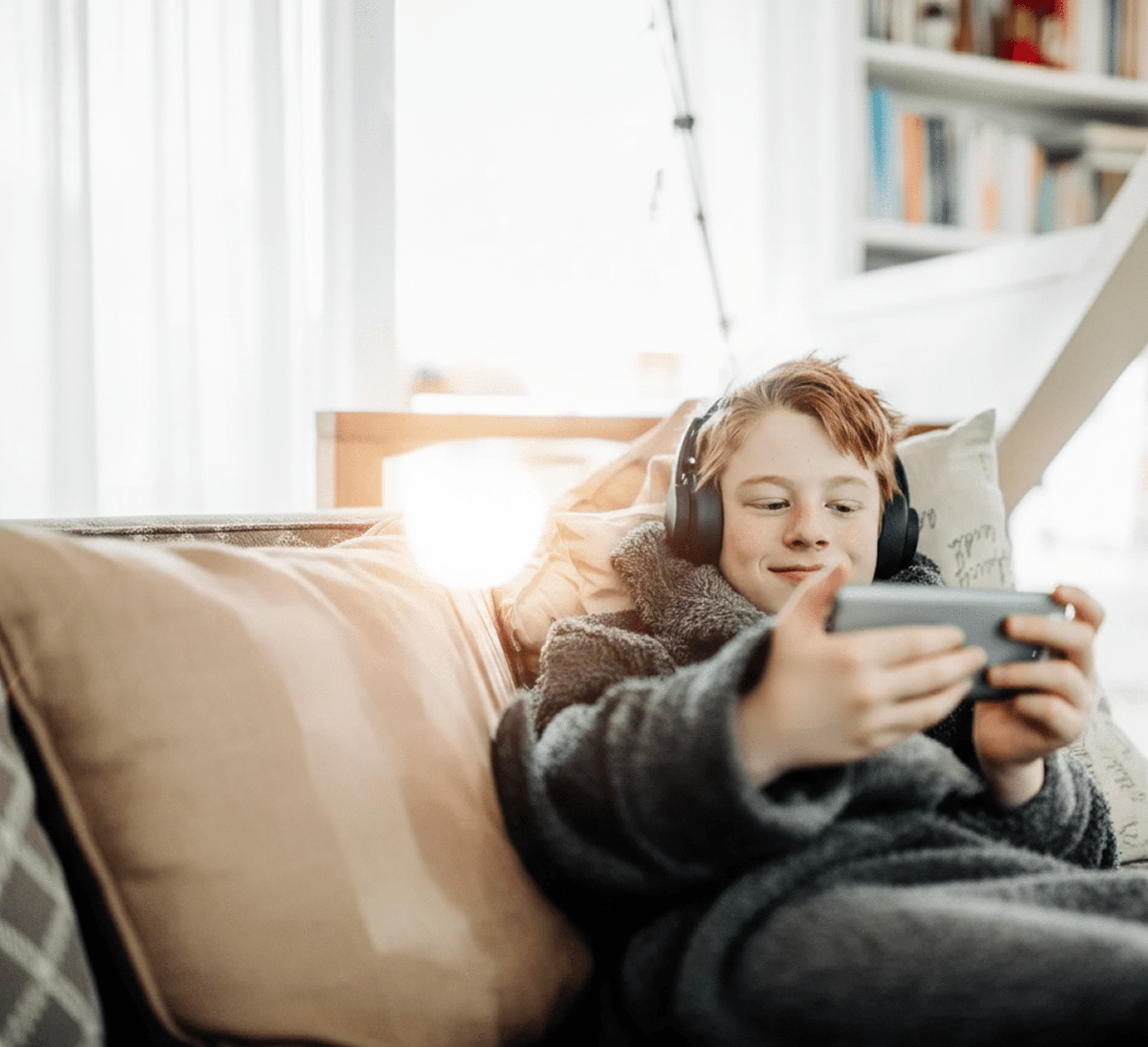 Ung gutt ligger på sofaen med headset og ser på mobilen