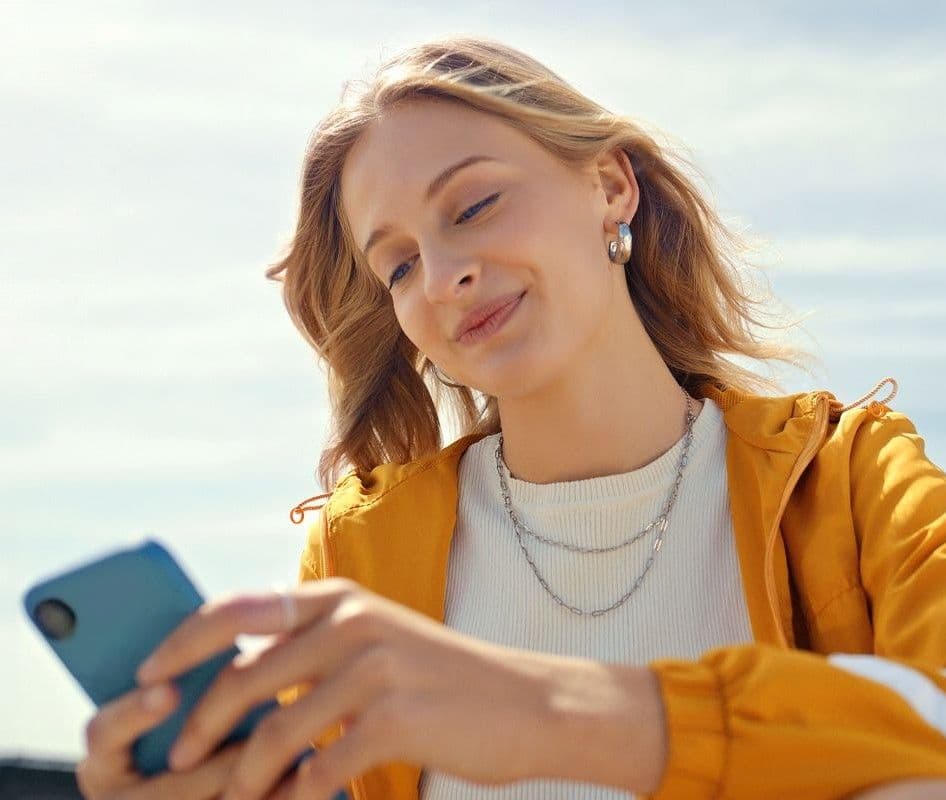 Ung kvinne sitter ut og ser på mobilen mens hun smiler