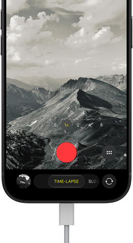 iPhone 18 Pro vises forfra. På skjermen er et fjellandskap, med kameramodus-overlay i tidsforløp-modus, med strømkabel festet til ladeporten