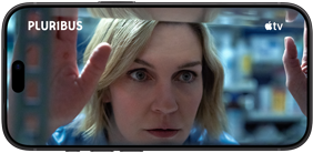 iPhone 18 Pro vises i liggende format, på skjermen er det et nærbilde av en kvinne som ser ut gjennom et vindu. Serietittel: Pluribus